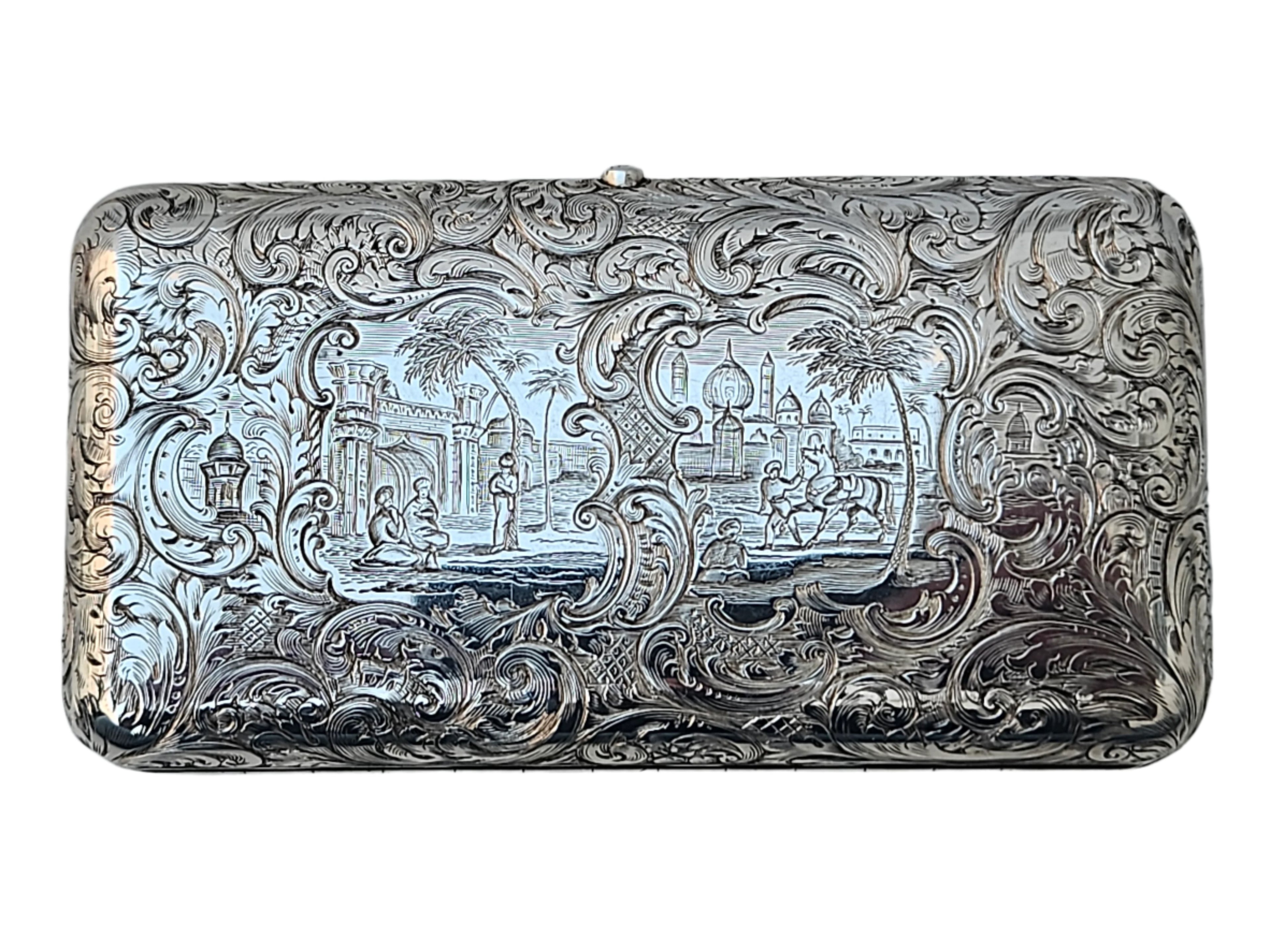 This sterling silver 19th-century antique English cigar box from Seventh Plateau features an intricately engraved scrollwork design. At its center, a scene unfolds showing a person near a gateway, surrounded by palm trees and domed buildings, all enriched with elaborate patterns. Its craftsmanship evokes the precision of an antique snuff box from Charles Rawlings & William Summers.