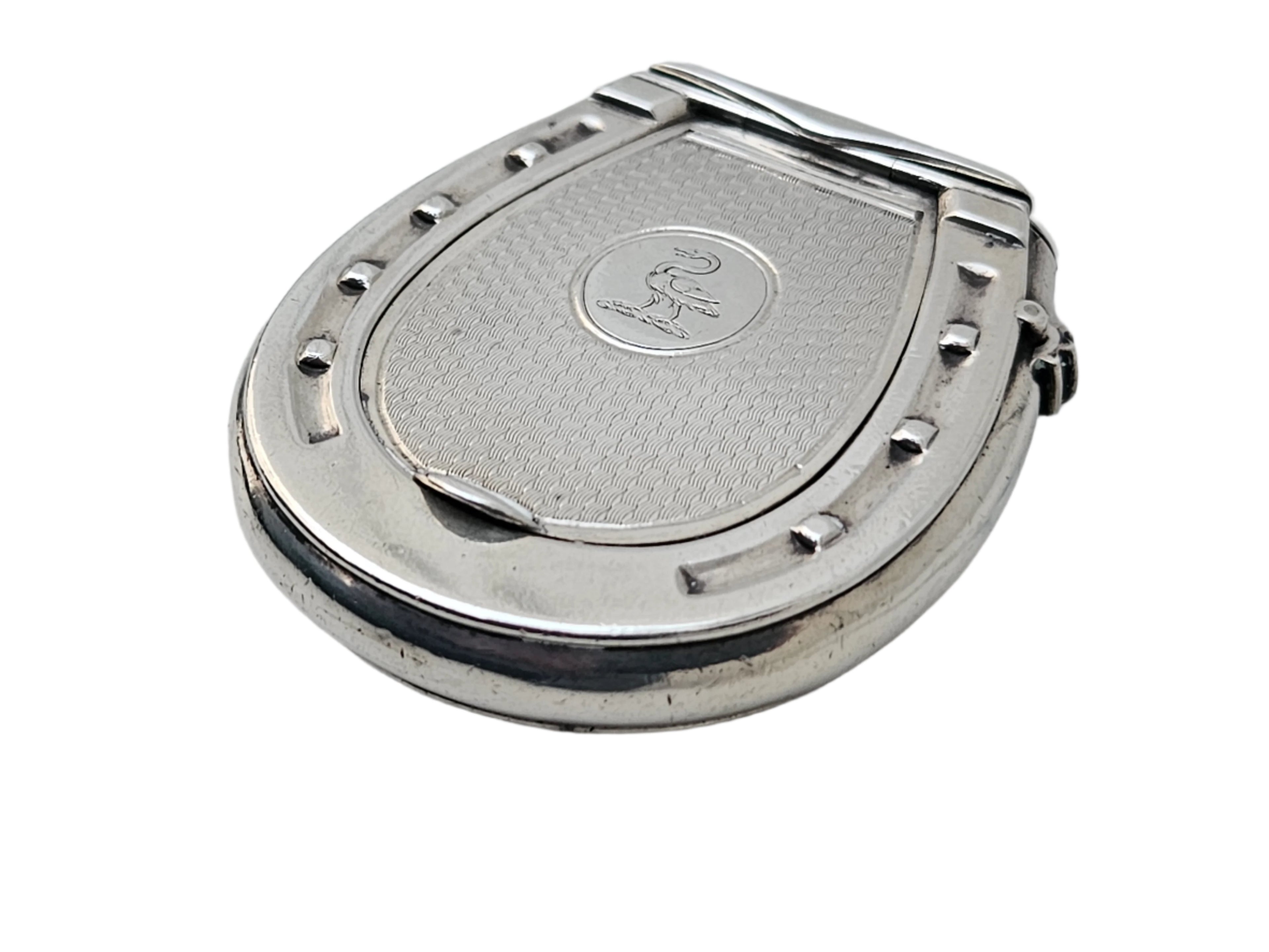 A STERLING SILVER 19TH CENTURY ANTIQUE FRENCH SNUFF BOX & VESTA MATCH CASE from SEVENTH PLATEAU, featuring a horseshoe shape with a textured surface and engraved logo, is elegantly displayed on a white marble background.