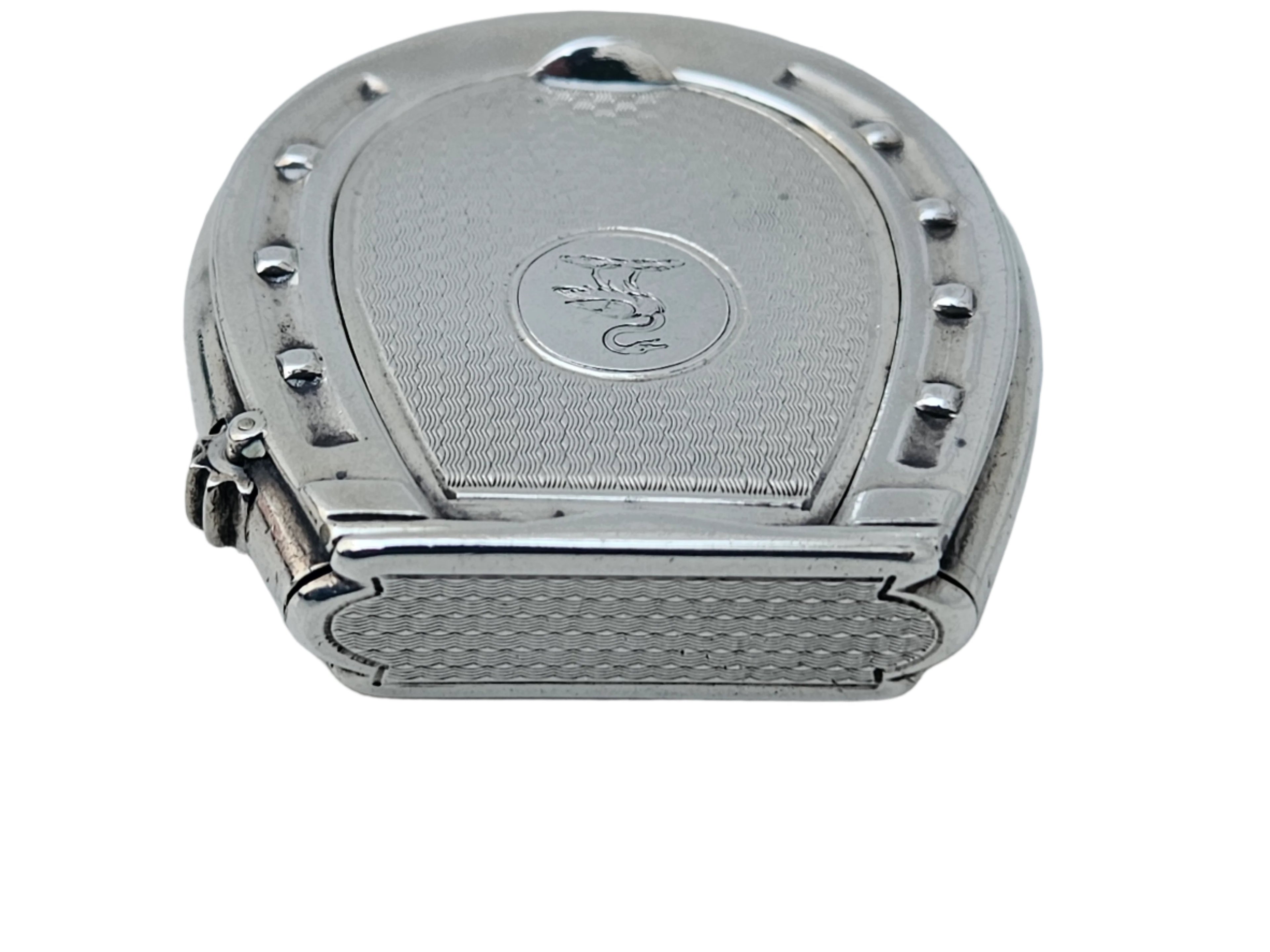 A STERLING SILVER 19TH CENTURY ANTIQUE FRENCH SNUFF BOX & VESTA MATCH CASE by SEVENTH PLATEAU, featuring a horseshoe design on top, rests on a light marble surface. It has a small engraved emblem in the center and intricate detailing around the edges.