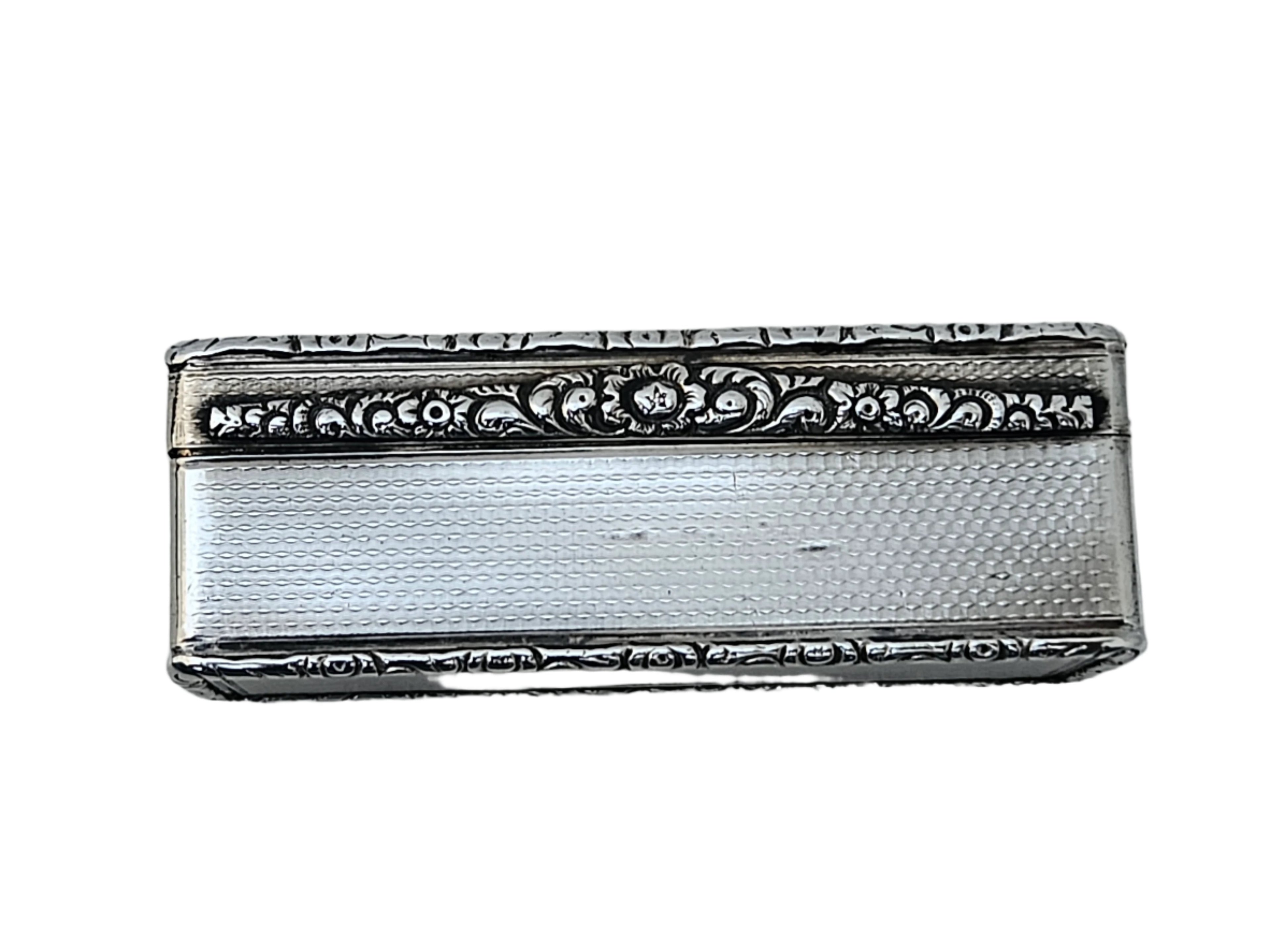 A rectangular sterling silver snuff box from SEVENTH PLATEAU, featuring intricate floral patterns and a textured surface, placed on a light marble background.